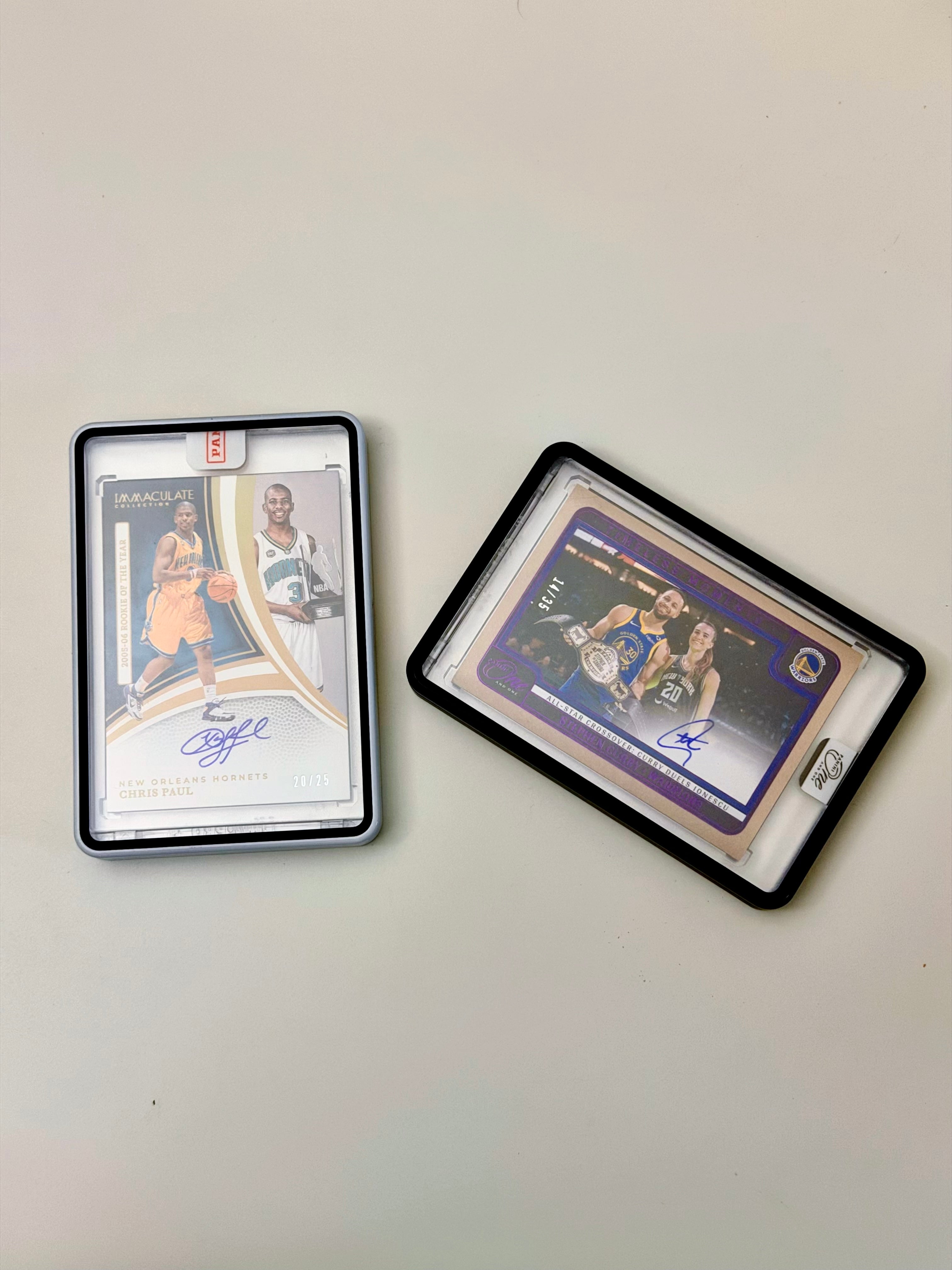 Two autographed basketball trading cards in protective cases, displayed on a plain off-white surface.